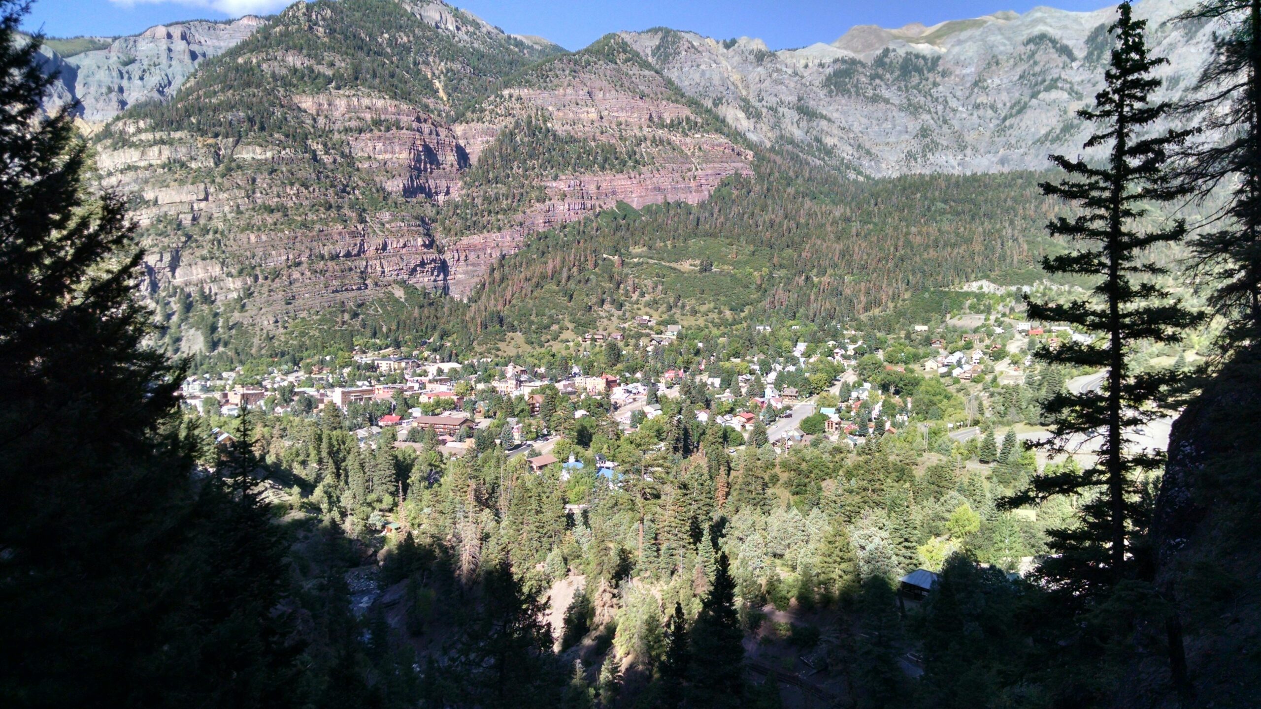 Beautiful aerial view of Ouray, Colorado surrounded by lush trees and majestic mountains under a clear sky.